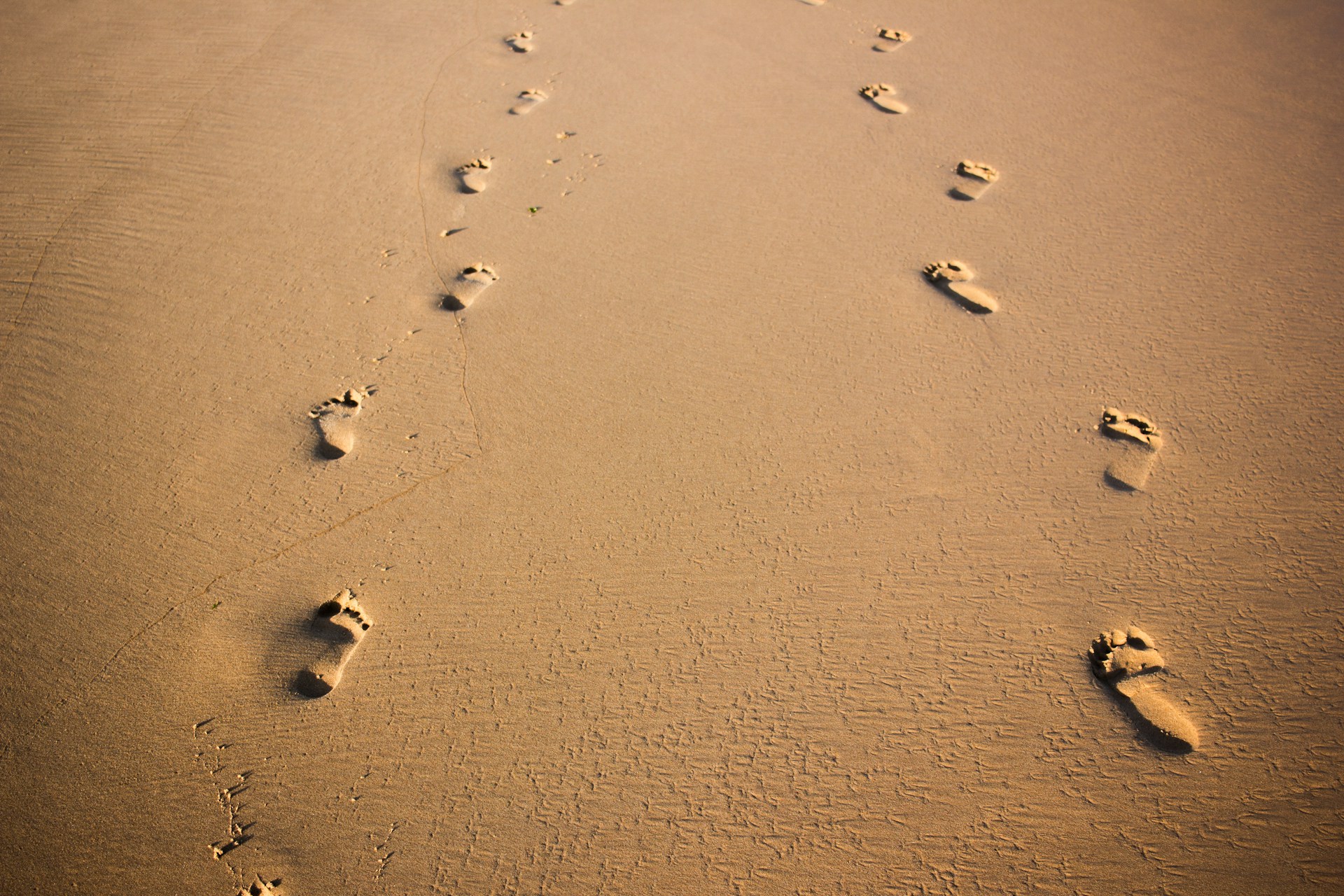 Foto van twee paar voetstappen in het zand.